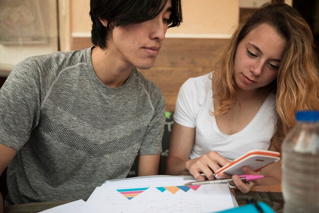 Pareja joven multirracial mirando en calculadora cerca de diagramas en papel