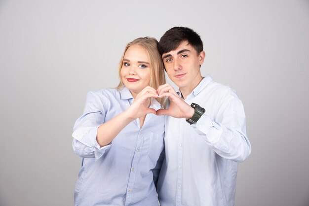 Pareja joven de novia y novio de pie juntos haciendo forma de símbolo de corazón con las manos.