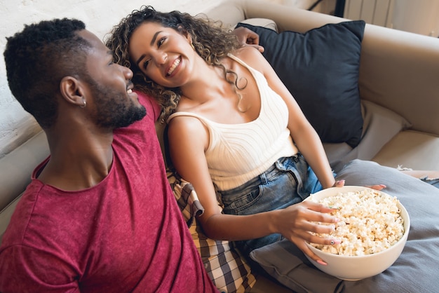 Pareja joven pasar tiempo juntos y ver series de televisión o películas mientras está sentado en el sofá en casa.