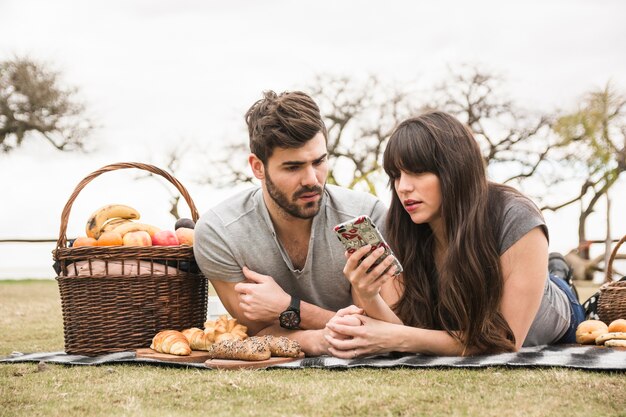 Pareja joven en picnic mirando el teléfono móvil