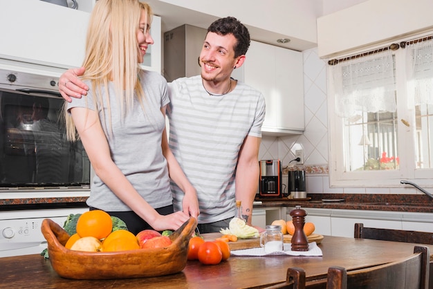 Pareja joven de pie detrás de la mesa de madera cortar verduras en la cocina