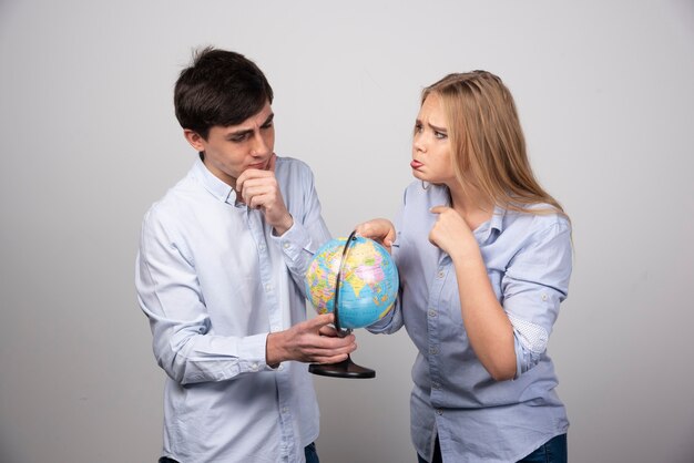 Pareja joven de pie con un globo terráqueo en pared gris