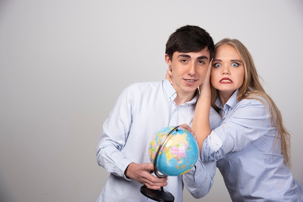 Pareja joven de pie con un globo terráqueo en pared gris