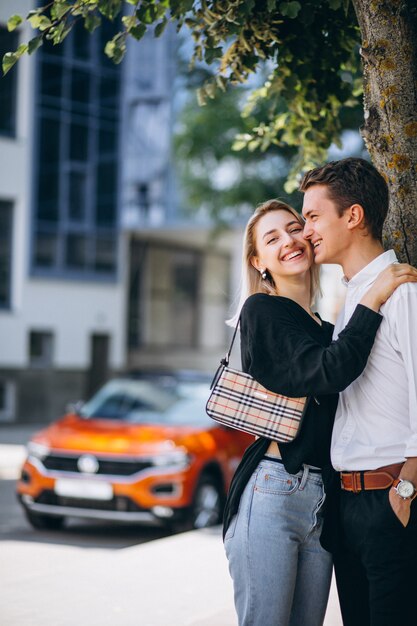 Pareja joven de pie junto a su auto nuevo