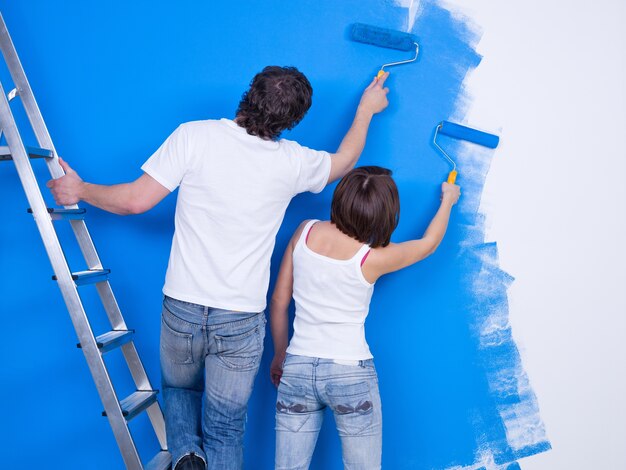 Pareja joven pintando la pared con rodillo juntos