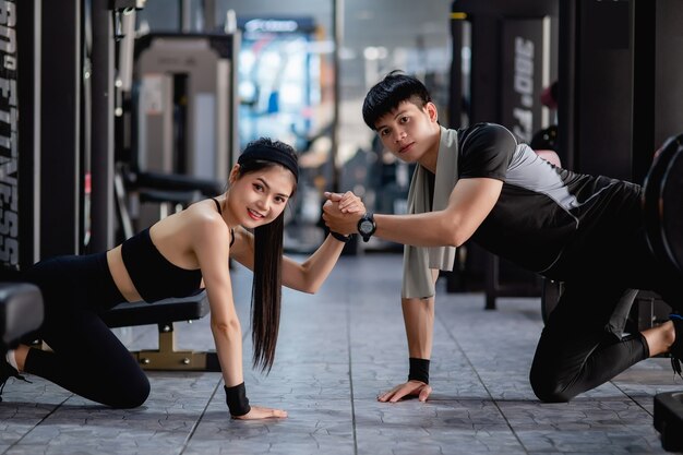 Pareja joven posan con la mano y mostrando músculos fuertes del brazo juntos en el gimnasio moderno,