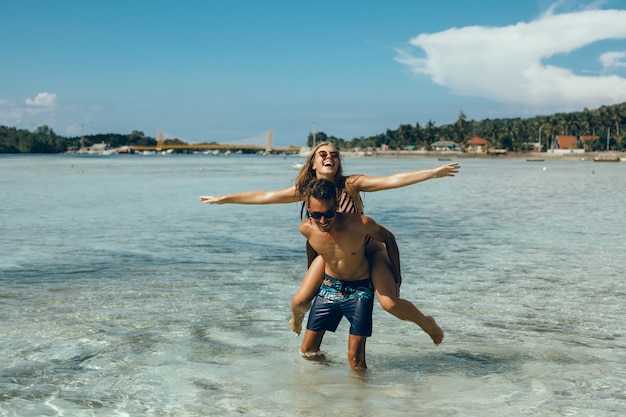 Pareja joven posando en la playa, divirtiéndose en el mar, riendo y sonriendo