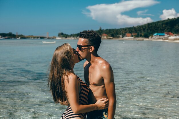 Pareja joven posando en la playa, divirtiéndose en el mar, riendo y sonriendo