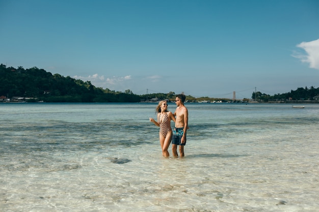 Pareja joven posando en la playa, divirtiéndose en el mar, riendo y sonriendo