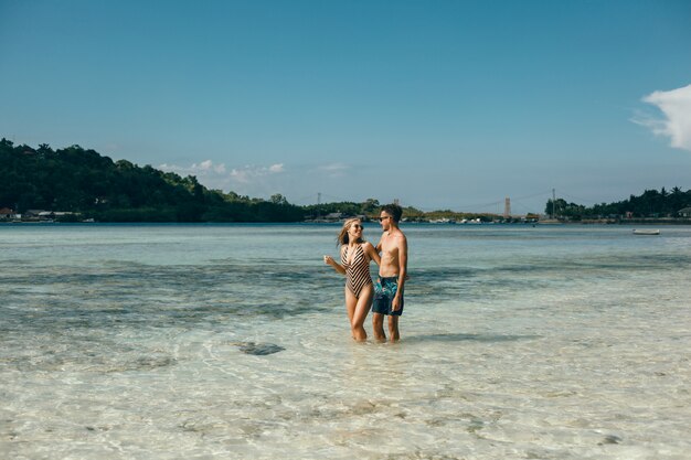 Pareja joven posando en la playa, divirtiéndose en el mar, riendo y sonriendo