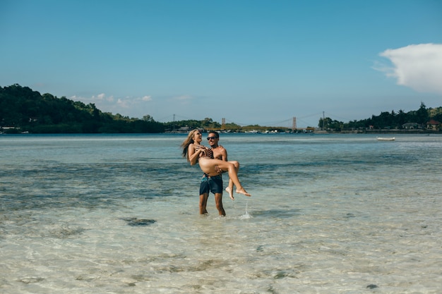 Pareja joven posando en la playa, divirtiéndose en el mar, riendo y sonriendo