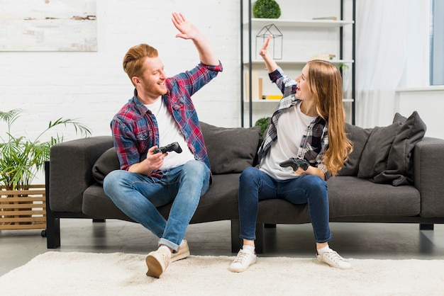 Pareja joven que da alta cinco mientras juega el videojuego en la sala de estar