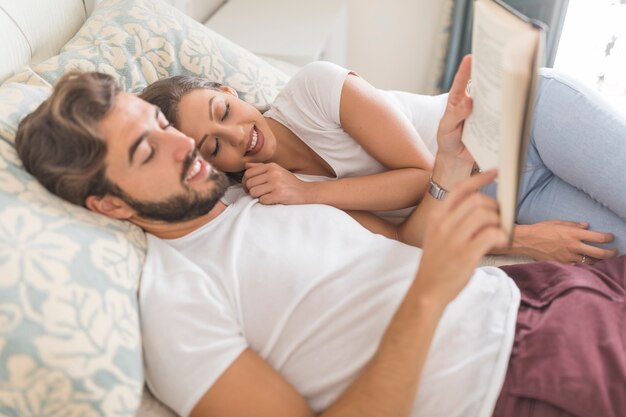 Pareja joven relajante con libro en la cama