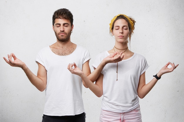 Pareja joven relajante meditando mientras está de pie contra la pared blanca