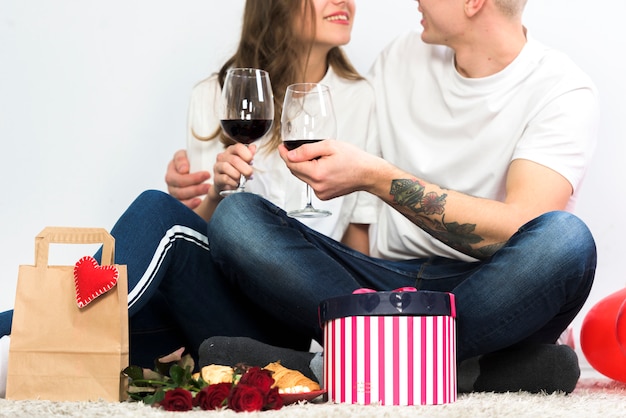 Pareja joven resonando copas de vino en el piso