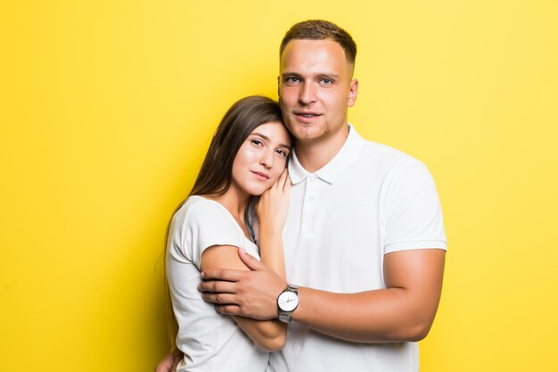 Pareja joven romántica aislada sobre fondo amarillo abrazándose juntos vestidos con camisetas blancas