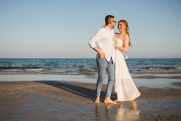 Pareja joven romántica mirando el uno al otro de pie cerca del mar en la playa