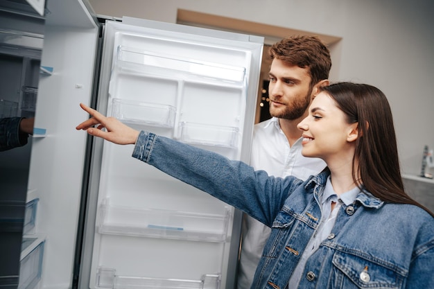 Pareja joven seleccionando refrigerador nuevo en la tienda de electrodomésticos