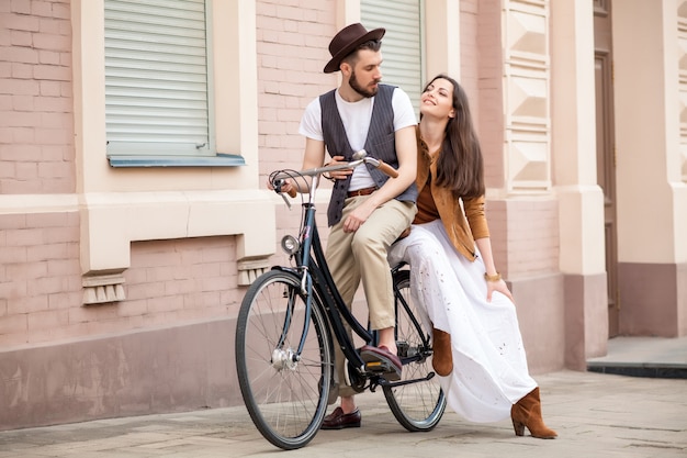 Pareja joven sentada en una bicicleta contra la pared