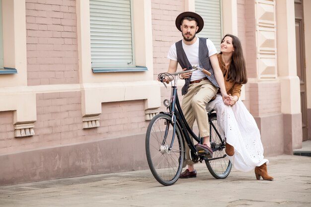 Pareja joven sentada en una bicicleta contra la pared