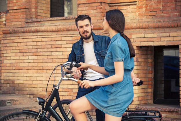 Pareja joven sentada en una bicicleta frente a la ciudad