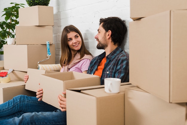 Pareja joven sentada entre las cajas de cartón mirando el uno al otro