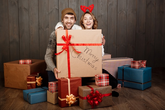 Pareja joven sentada entre cajas de regalo de Navidad sobre superficie de madera