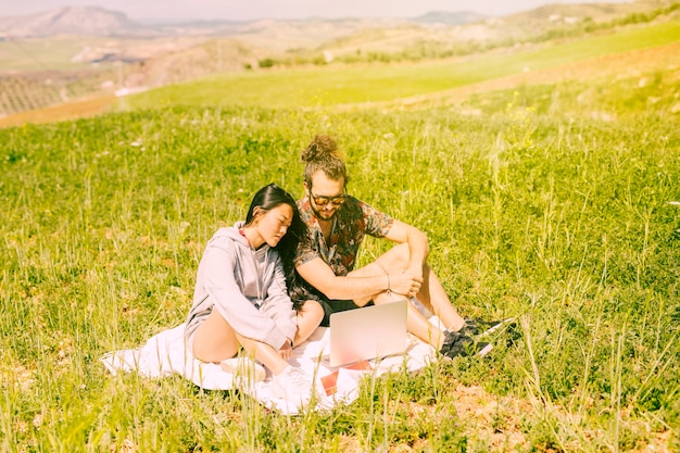 Foto gratuita pareja joven sentada en el campo con el portátil