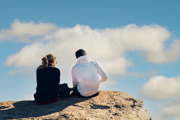 Pareja joven sentada en la cima de un acantilado bajo un cielo nublado