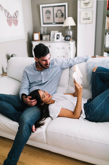 Pareja joven sentada en el libro de lectura de sofá blanco