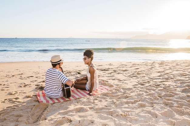 Pareja joven sentada en la playa con guitarra