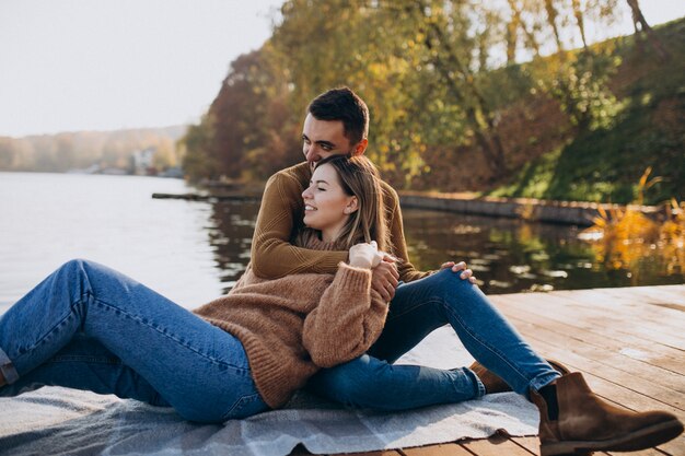 Pareja joven sentada en el puente de cubierta junto al río