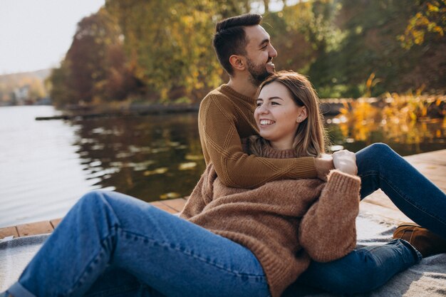 Pareja joven sentada en el puente de cubierta junto al río