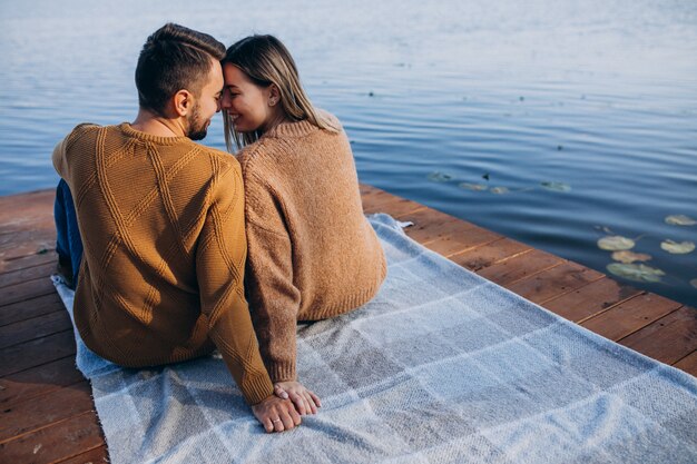 Pareja joven sentada en el puente de cubierta junto al río