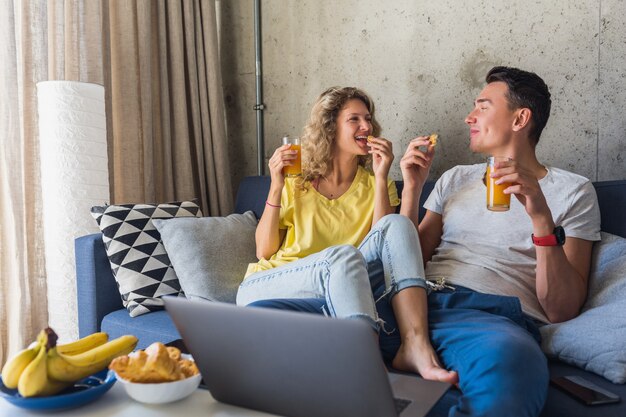 Pareja joven sentada en el sofá en casa desayunando en la mañana