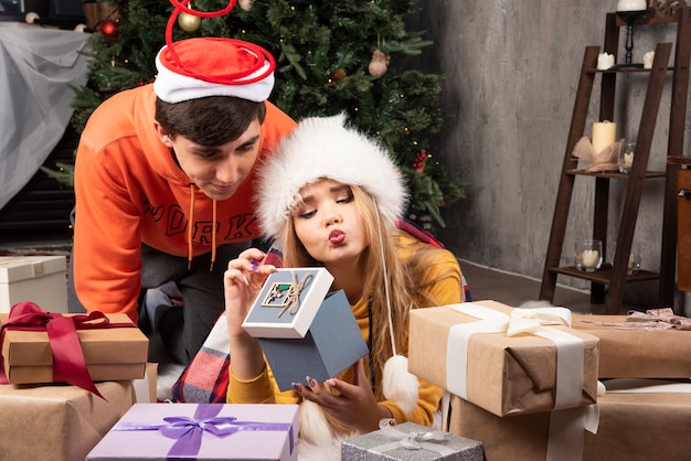 Pareja joven sentada en el suelo y abriendo regalos cerca del árbol de Navidad