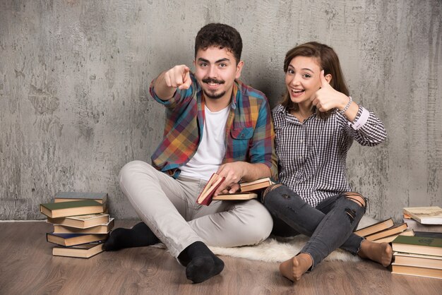 Pareja joven sentada en el suelo con libros y apuntando al frente