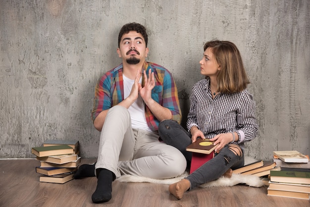 pareja joven sentada en el suelo con libros