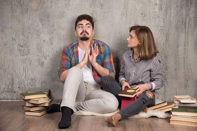 pareja joven sentada en el suelo con libros