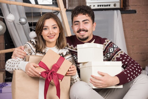 Pareja joven sentada en el suelo con regalos de Navidad en sala festiva.