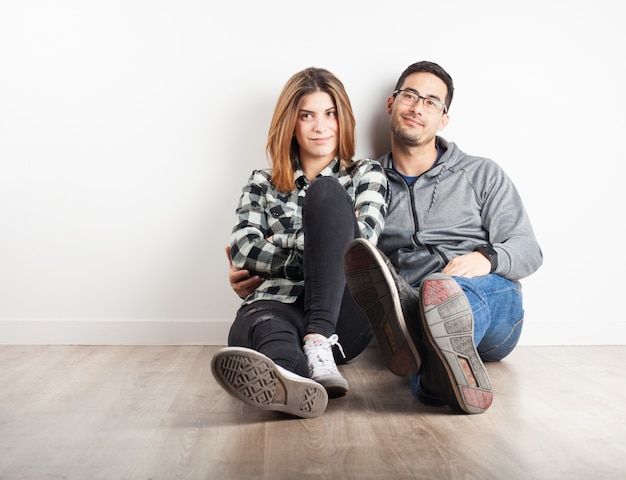 Foto gratuita pareja jóven sentada en el suelo sonriendo