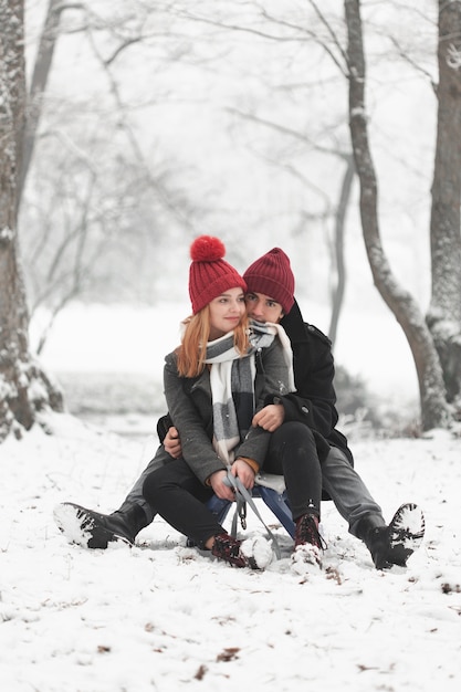 Pareja joven sentada en trineo en invierno