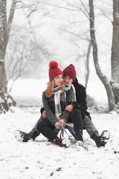 Pareja joven sentada en trineo en invierno