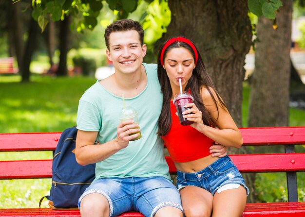 Pareja joven sentado en el banco bebiendo batidos saludables en el parque