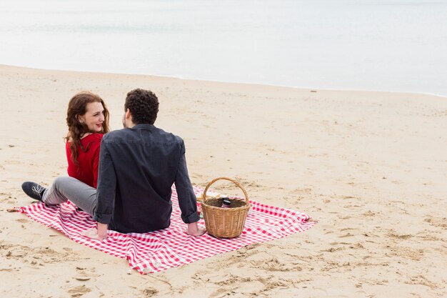 Pareja joven, sentado, en, coverlet, en, orilla de mar