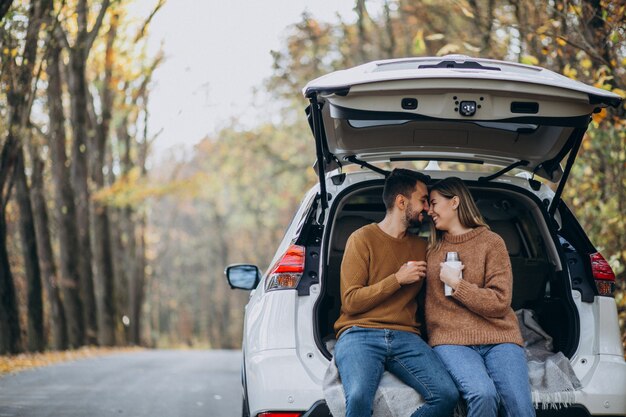 Pareja joven sentado en la parte trasera de un coche bebiendo té en el bosque