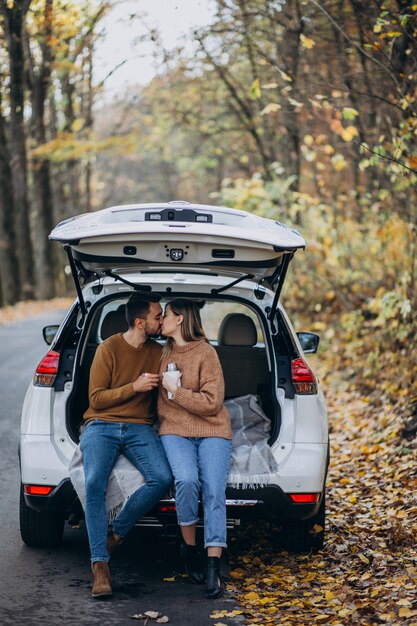 Pareja joven sentado en la parte trasera de un coche bebiendo té en el bosque