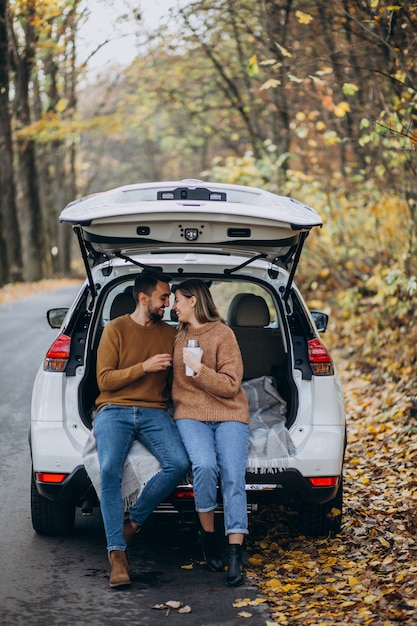 Pareja joven sentado en la parte trasera de un coche bebiendo té en el bosque