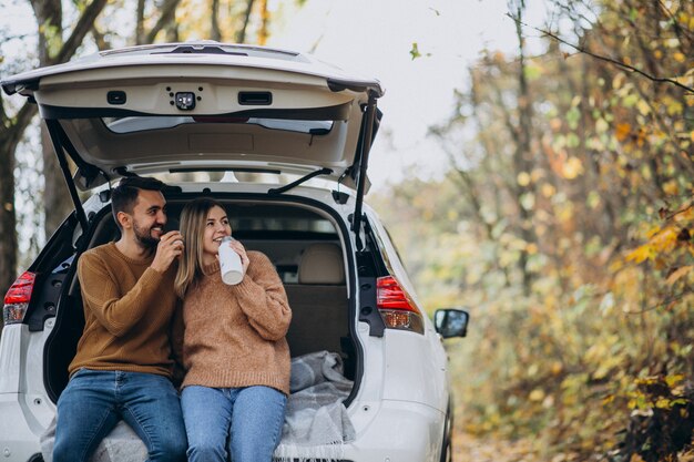 Pareja joven sentado en la parte trasera de un coche bebiendo té en el bosque