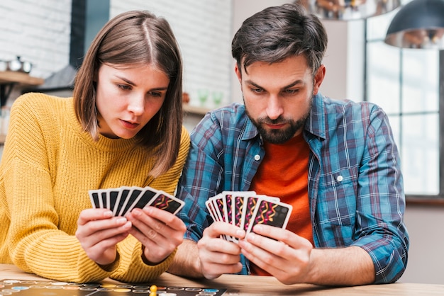 Pareja joven seria mirando sus cartas jugando el juego de mesa